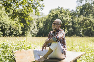 Lächelnder älterer Mann mit Brille sitzt auf einem Picknicktisch - UUF26532