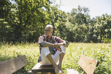 Älterer Mann sitzt auf einem Picknicktisch im Park - UUF26534