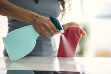 Hand einer Frau, die zu Hause einen Tisch reinigt und Wasser versprüht - JSRF02104