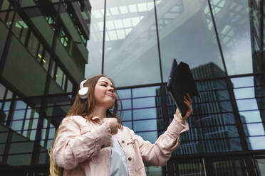 Smiling woman with tablet PC in front of glass building - IHF00927