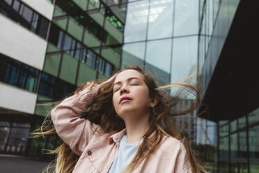 Junge Frau mit geschlossenen Augen vor einem Gebäude stehend - IHF00932