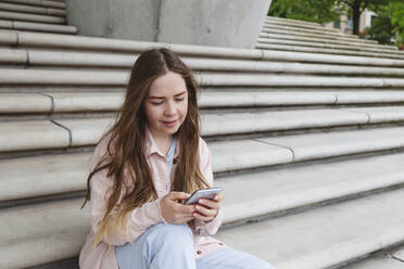 Lächelnde junge Frau mit Smartphone auf einer Treppe sitzend - IHF00942