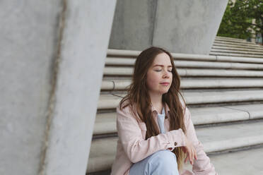 Junge Frau mit geschlossenen Augen auf einer Treppe sitzend - IHF00944