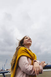 Smiling young woman standing under cloudy sky - IHF00946