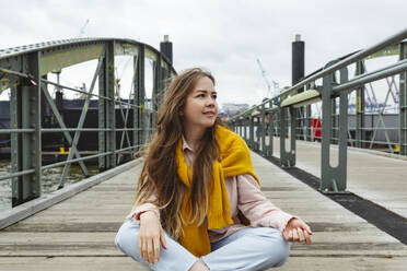 Smiling young woman with long brown hair sitting on footbridge - IHF00950