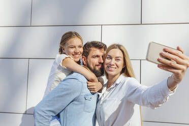 Glückliche Frau nimmt Selfie mit Familie durch Smartphone vor der Wand - IHF00971