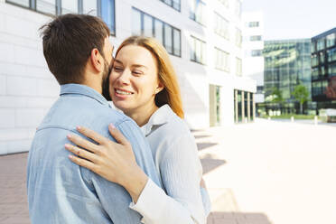 Happy man and woman hugging each other on sunny day - IHF00984