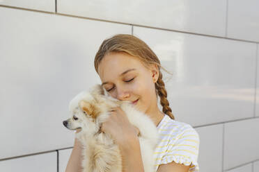 Lächelndes Mädchen umarmt Hund vor einer Mauer - IHF00987