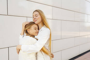 Happy mother hugging daughter in front of wall - IHF00989
