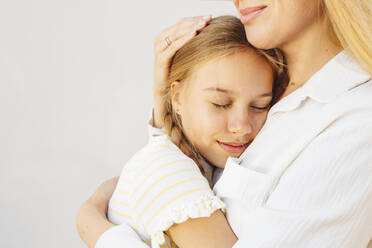 Smiling woman hugging daughter in front of wall - IHF00990