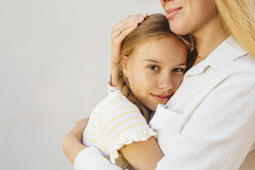 Smiling blond woman hugging daughter in front of wall - IHF00991