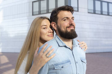 Lächelnde Frau mit langen Haaren steht hinter einem Mann vor einem Gebäude - IHF01007