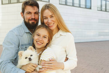 Glückliche Familie mit Hund vor einem Gebäude stehend - IHF01009