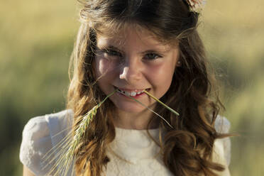 Smiling girl holding wheat crop in mouth - JCMF02310