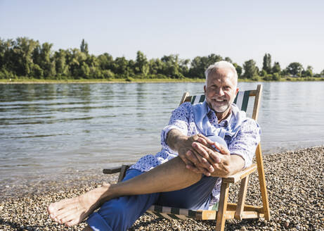 Lächelnder älterer Mann am Flussufer an einem sonnigen Tag - UUF26544