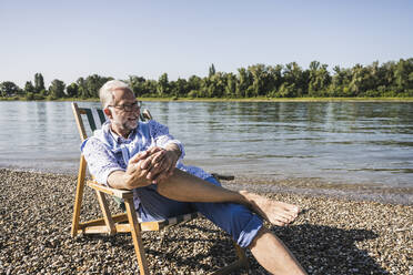 Smiling senior man wearing eyeglasses at riverbank - UUF26545