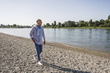 Man with hands in pocket walking at riverbank - UUF26582