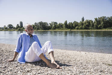 Smiling senior man sitting at riverbank - UUF26609