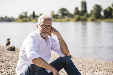 Mann sitzt am Flussufer an einem sonnigen Tag - UUF26615