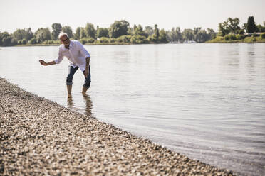 Verspielter älterer Mann wirft Kieselsteine in den Fluss - UUF26619