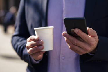 Hands of businessman holding disposable cup and smart phone - JOSEF10601