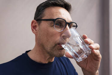 Businessman wearing eyeglasses drinking water in glass - JOSEF10634