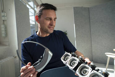 Smiling engineer holding virtual reality headset looking at lighting equipment at office - JOSEF10635