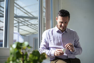 Businessman having coffee by window at office - JOSEF10662