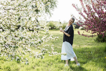 Happy woman holding white flowers standing in garden - LLUF00687