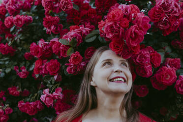 Glückliche Frau steht unter einer Pflanze mit roten Rosen - OSF00133