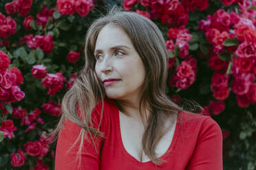 Thoughtful woman in front of red rose bush - OSF00135