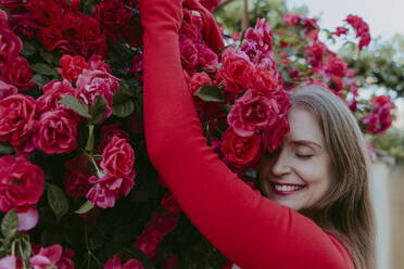 Happy woman with eyes closed embracing rose bush - OSF00141