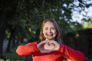 Happy woman with brown hair gesturing heart shape - OSF00144