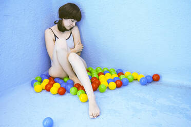 Traurige Frau sitzt inmitten von bunten Bällen an einer blauen Schwimmbadwand - SVCF00099