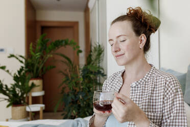 Woman with eyes closed sitting with cup of tea at home - TYF00280