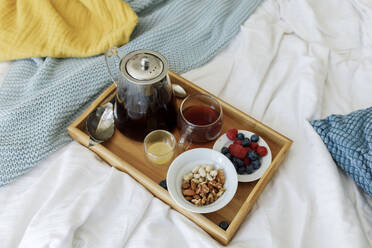 Tea pot in wooden tray with berries and nuts on bed - TYF00281