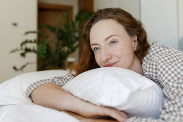 Lächelnde Frau auf dem Bett liegend mit Kissen im Schlafzimmer - TYF00286