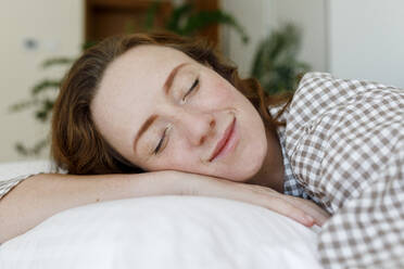 Lächelnde Frau entspannt sich auf einem Kissen im Schlafzimmer - TYF00288