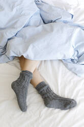 Beine einer Frau in kuscheligen Socken unter einer Decke auf dem Bett - TYF00296