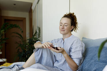 Woman with eyes closed sitting with cup of tea at home - TYF00300