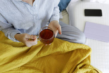 Frau mit Tasse Tee auf dem Bett sitzend - TYF00301