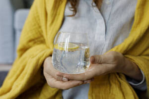 Hände einer Frau, die kohlensäurehaltiges Wasser mit einer Zitronenscheibe im Glas hält - TYF00310