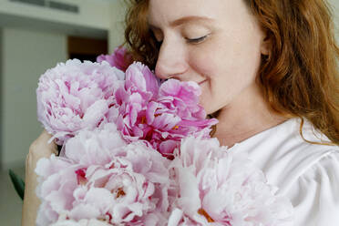 Smiling woman smelling pink flowers at home - TYF00336