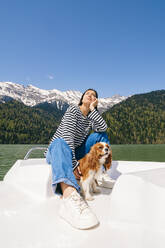 Frau mit Hund genießt den sonnigen Tag auf einem Boot auf dem Ritsa-See - OMIF00901