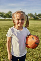 Lächelndes blondes Mädchen mit Rugbyball an einem sonnigen Tag - ZEDF04640