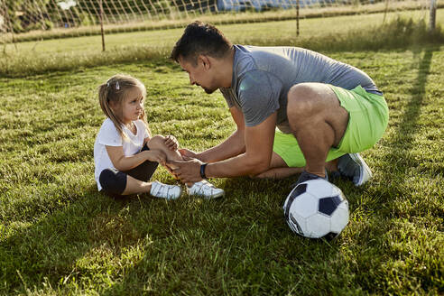 Father consoling injured daughter sitting at sports field - ZEDF04651