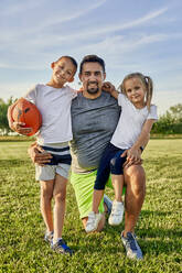 Glücklicher Mann mit Tochter und Sohn, die einen Rugbyball auf einem Sportplatz halten - ZEDF04661