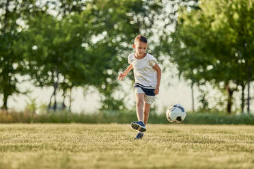 Junge spielt Fußball auf einem Sportplatz an einem sonnigen Tag - ZEDF04667