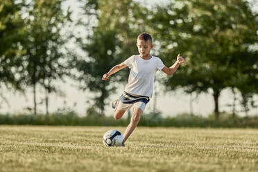 Junge kickt Fußball auf einem Sportplatz an einem sonnigen Tag - ZEDF04672