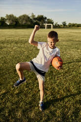 Boy with rugby ball doing haka dance standing on one leg at sports field - ZEDF04678